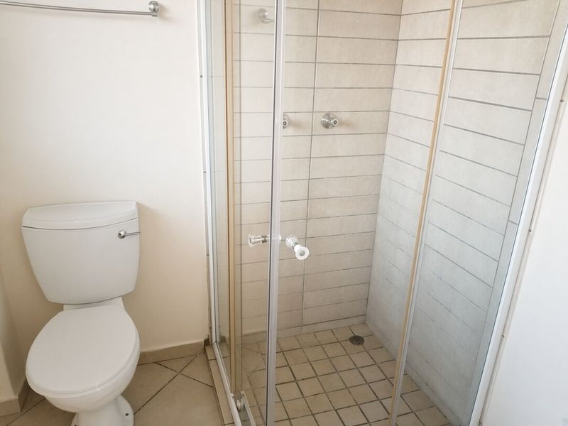 A functional bathroom featuring a white toilet and a glass-enclosed shower with neutral wall and floor tiling.