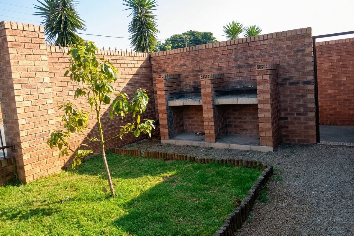 A private rear courtyard featuring a built-in brick braai, established lawn, and secure brick boundary walls.