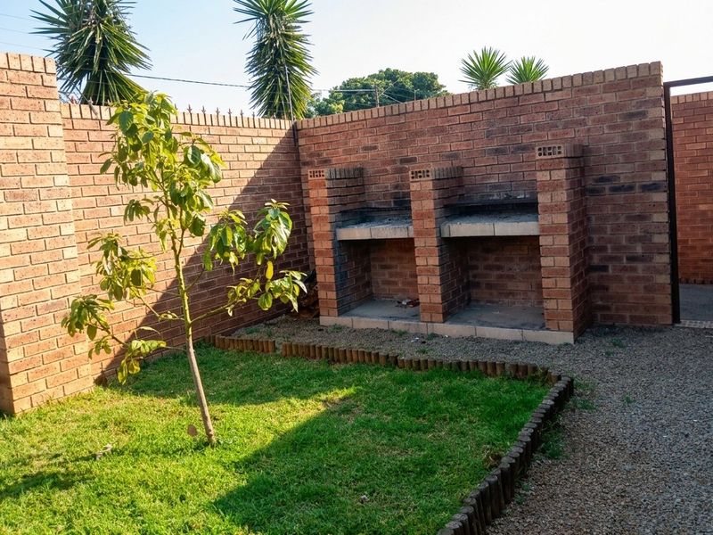 A private rear courtyard featuring a built-in brick braai, established lawn, and secure brick boundary walls.