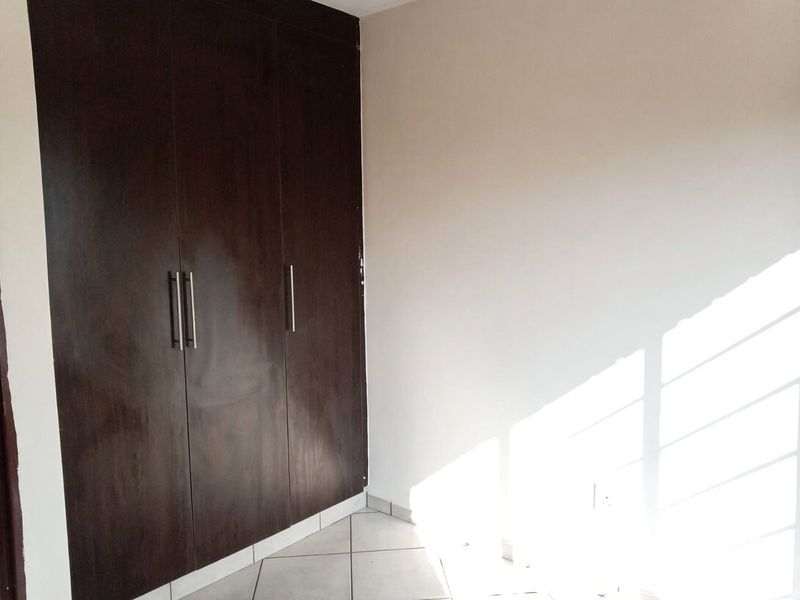 A bright, empty bedroom featuring dark wood built-in cupboards and neutral tiled flooring.