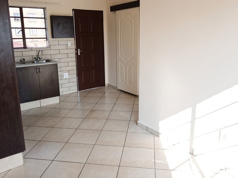 A compact, empty kitchen area featuring dark cabinetry, a stainless steel sink, tiled backsplash, and neutral floor tiles, ready for personalization.