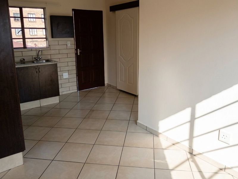 An open-plan living area featuring tiled flooring, a compact kitchen corner with cabinetry and sink, and access to a sliding door.