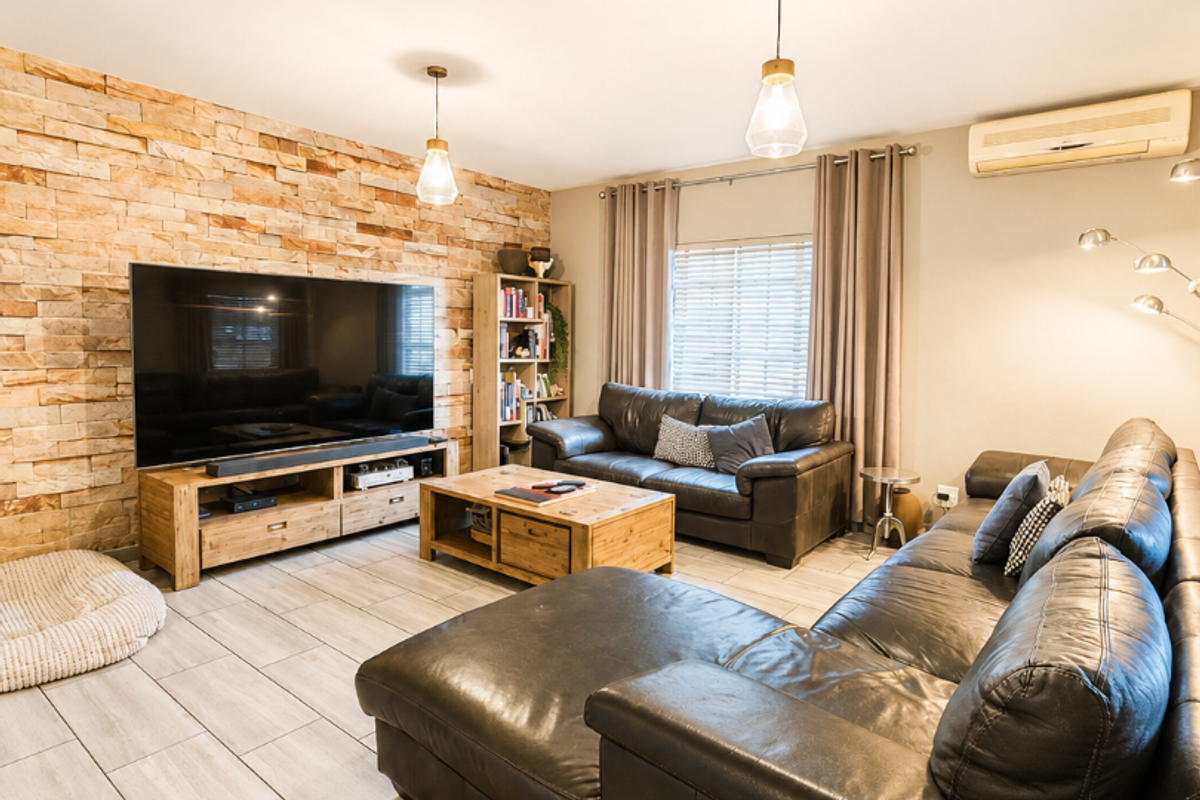 A well-maintained living room featuring a textured stone feature wall, neutral tiled flooring, and a wall-mounted split-system air conditioner.