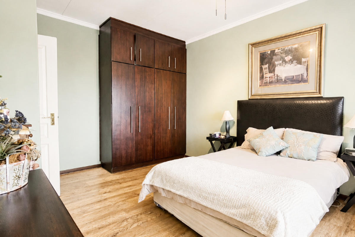 A well-maintained bedroom featuring light-toned laminate flooring, a dark wood built-in wardrobe, and a modern ceiling fan.