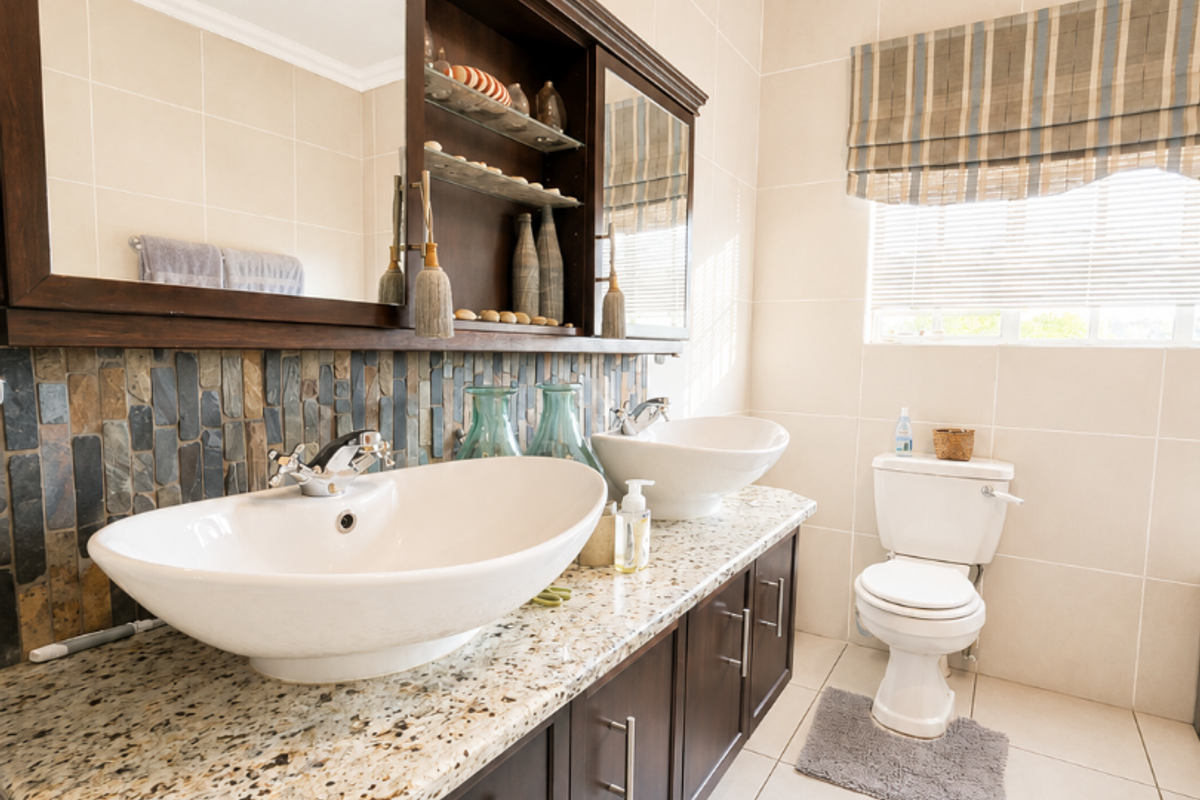A well-maintained bathroom featuring a double vanity with granite countertops, vessel sinks, built-in cabinetry, and neutral wall and floor tiling.