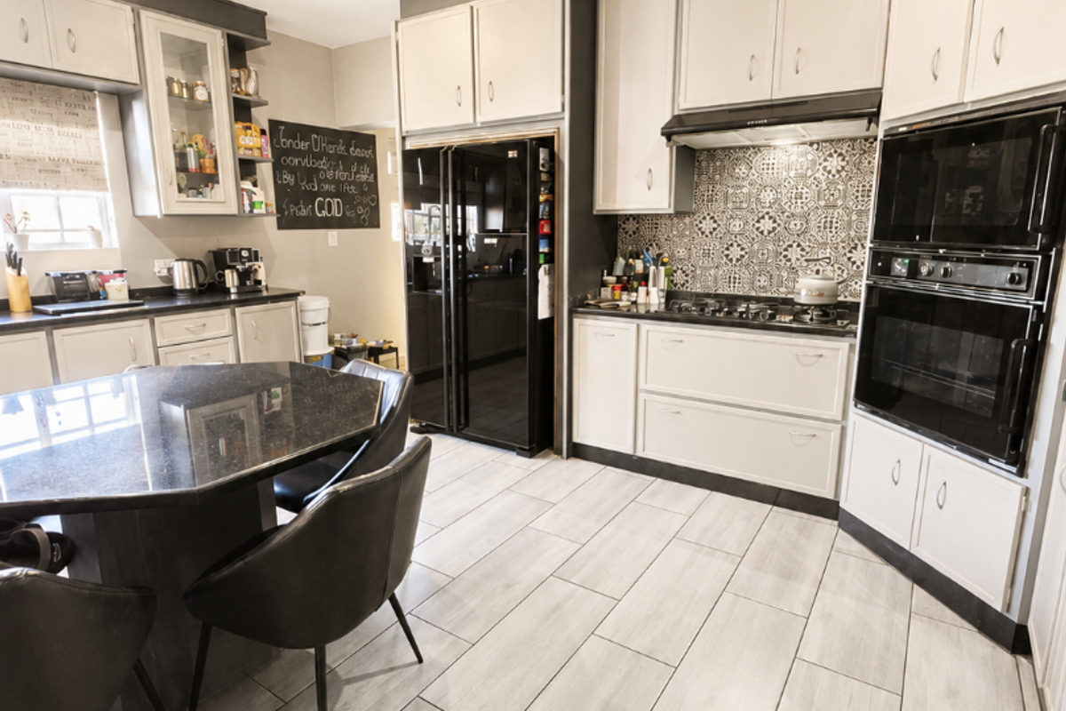 Modern kitchen featuring light-toned cabinetry, granite countertops, a decorative tiled backsplash, and integrated appliances including a gas hob and double oven.