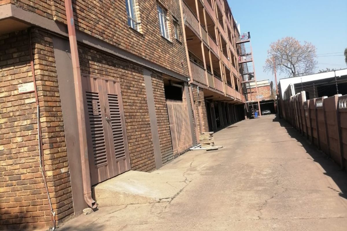 Exterior view of an apartment building featuring a face brick facade, concrete driveway, and rear access area with metal security gates.