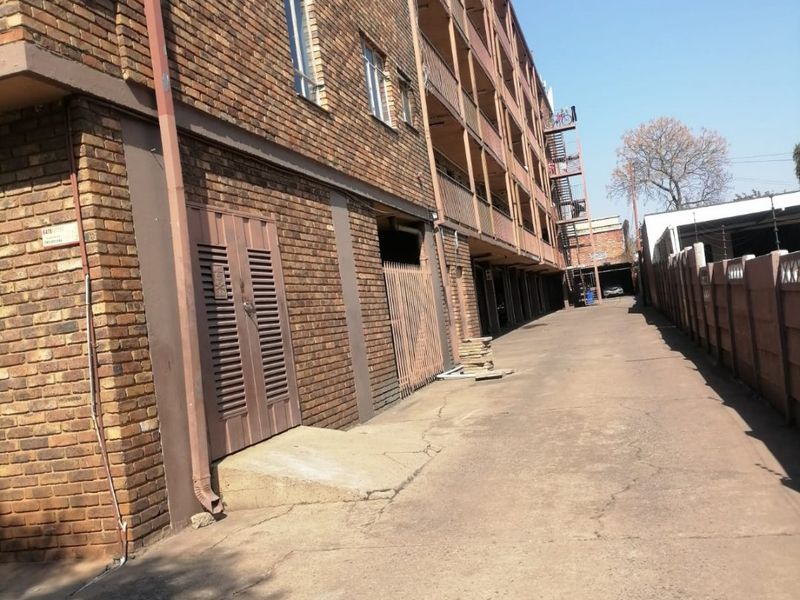 Exterior view of an apartment building featuring a face brick facade, concrete driveway, and rear access area with metal security gates.