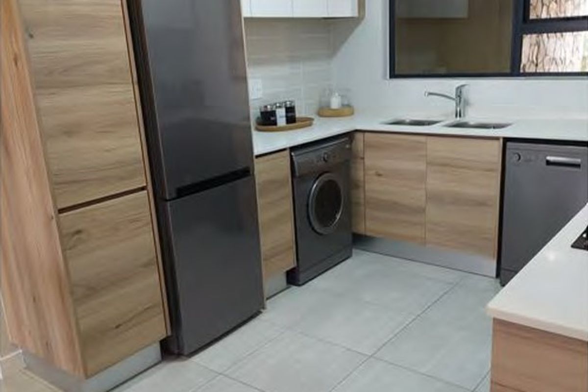 Modern kitchen featuring light wood-grain cabinetry, stone countertops, integrated appliances, and large format floor tiles.