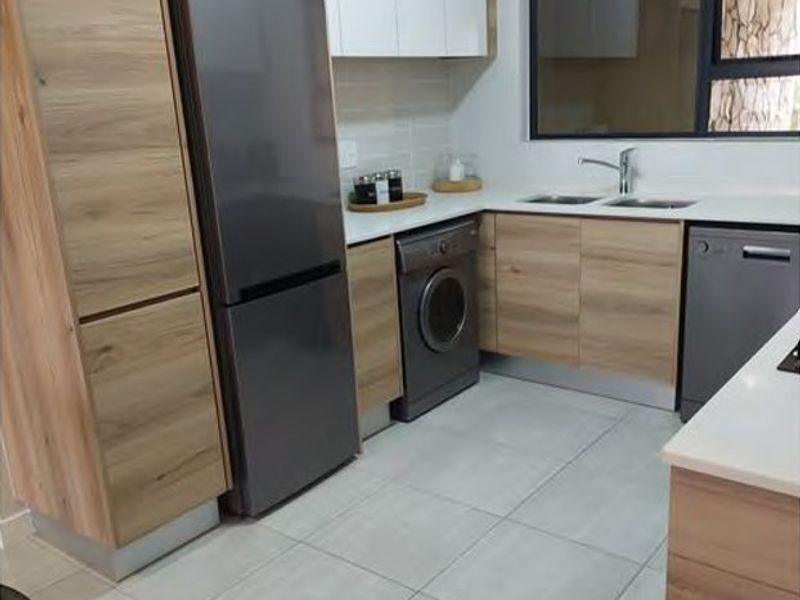 Modern kitchen featuring light wood-grain cabinetry, stone countertops, integrated appliances, and large format floor tiles.
