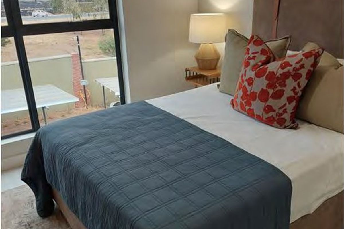A well-lit bedroom featuring a large window with a view, neutral wall finishes, and modern architectural design.