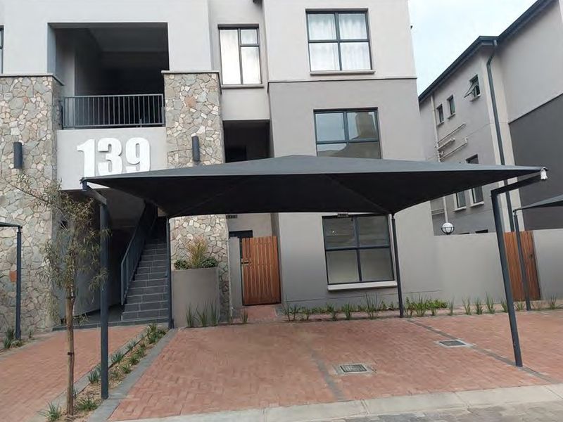 Front elevation of a modern apartment building featuring stone cladding, a paved driveway, and a dedicated shade sail carport.