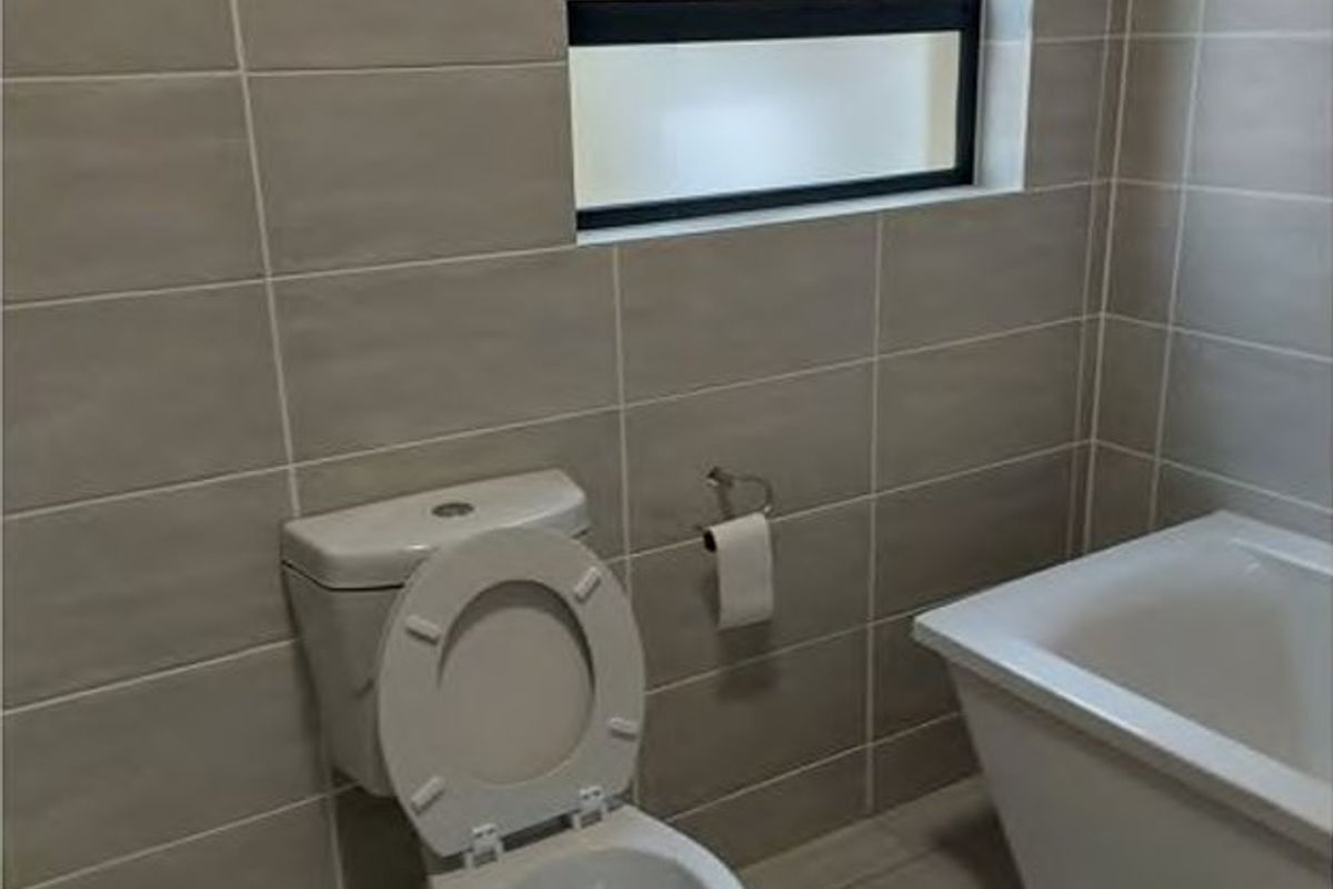 A clean, modern bathroom featuring neutral wall and floor tiles, a white bathtub, and a top-hung window for natural light and ventilation.