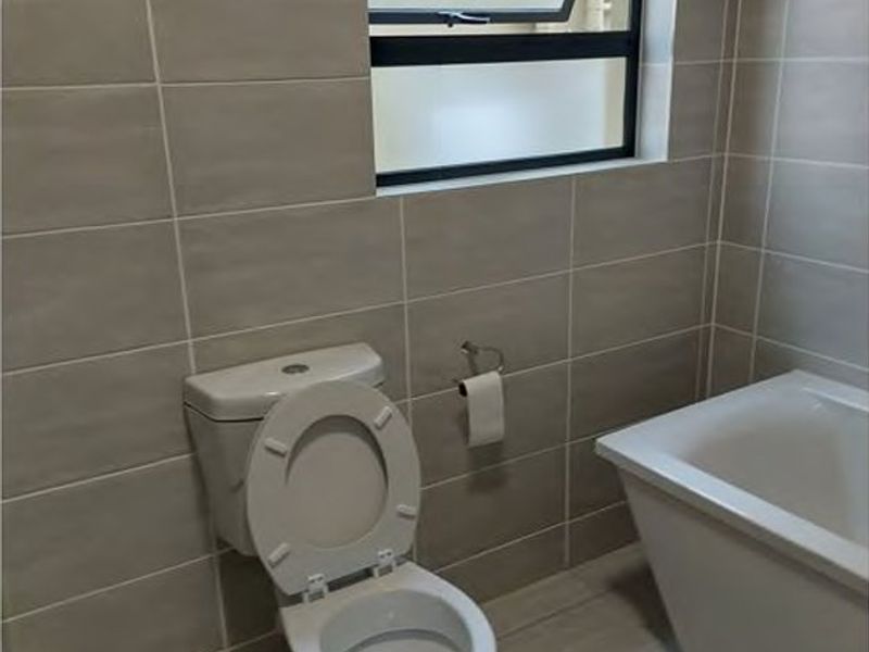 A clean, modern bathroom featuring neutral wall and floor tiles, a white bathtub, and a top-hung window for natural light and ventilation.