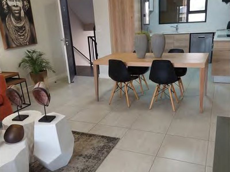An open-plan living and dining area featuring tiled flooring, leading into a functional kitchen with built-in cabinetry and integrated appliances.