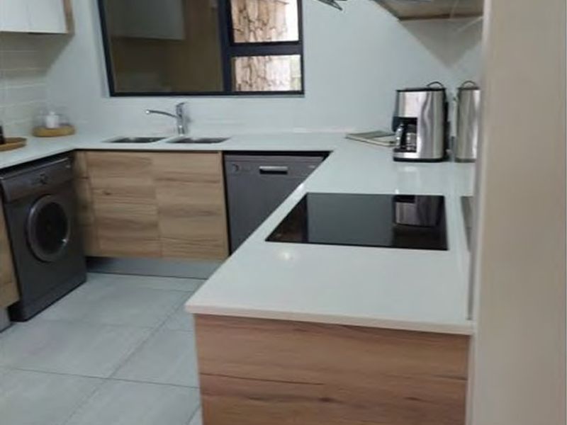 Modern kitchen featuring wood-finish cabinetry, stone countertops, integrated hob, extractor fan, and tiled flooring in a clean, functional layout.