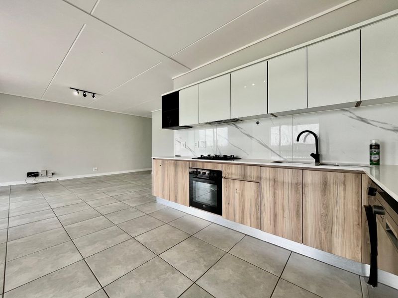 Modern open-plan kitchen featuring wood-grain cabinetry, white high-gloss upper cupboards, marble-look splashback, and integrated appliances, flowing into a spacious living area with tiled floors.