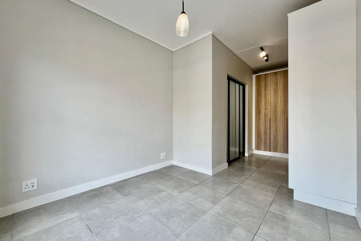 A bright, empty living area featuring neutral tiled flooring, modern pendant lighting, and built-in wooden cabinetry.