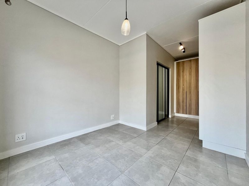 A bright, empty living area featuring neutral tiled flooring, modern pendant lighting, and built-in wooden cabinetry.