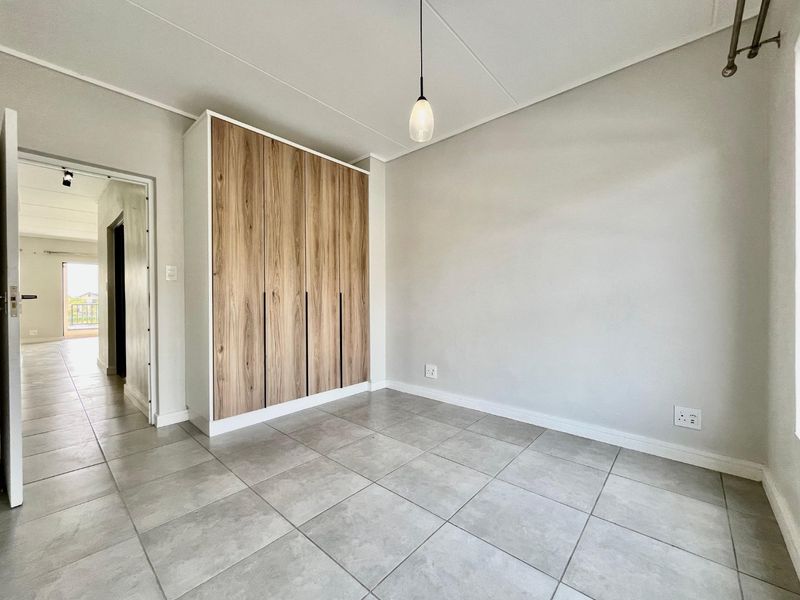 A bright, empty bedroom featuring modern wood-finish built-in wardrobes, neutral tiled flooring, and a contemporary pendant light fixture.