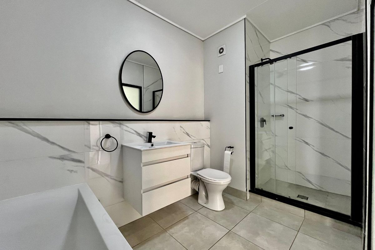 Modern bathroom featuring a sleek vanity, walk-in shower with black frame, marble-look wall tiles, and neutral floor tiling.