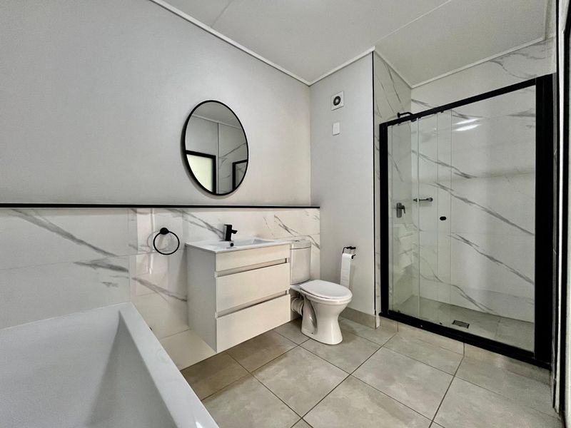 Modern bathroom featuring a sleek vanity, walk-in shower with black frame, marble-look wall tiles, and neutral floor tiling.