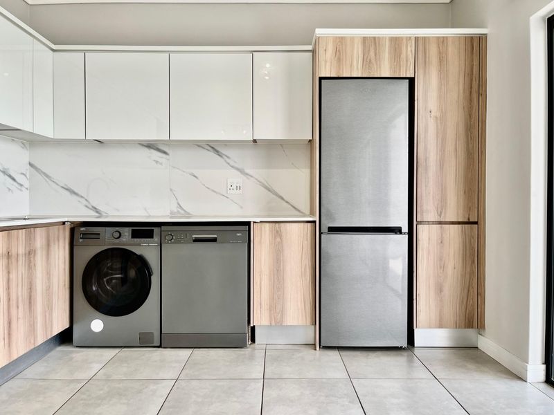 Modern kitchen featuring sleek white and wood-grain cabinetry, marble-look splashback, and integrated appliance housing with tiled flooring.