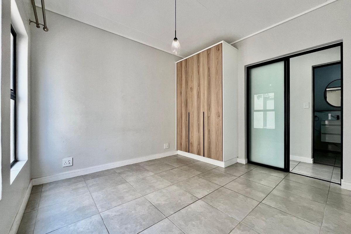 A bright, modern bedroom featuring neutral tiled flooring, a contemporary built-in wardrobe with wood-grain finish, and a sleek sliding glass door.