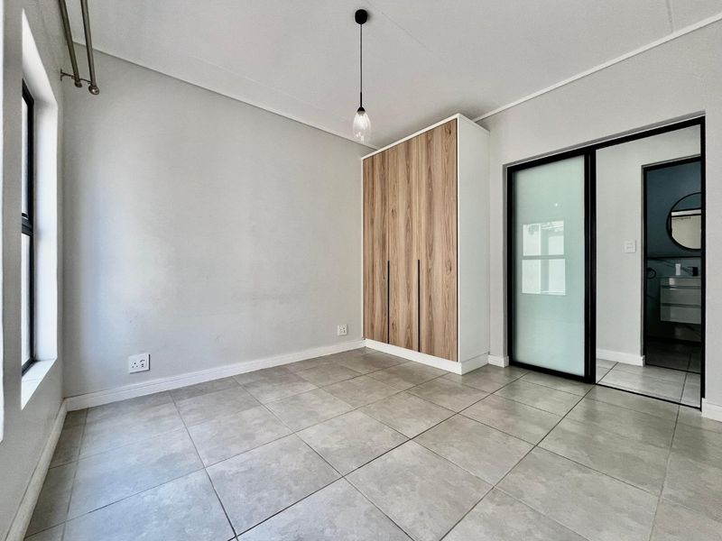 A bright, modern bedroom featuring neutral tiled flooring, a contemporary built-in wardrobe with wood-grain finish, and a sleek sliding glass door.