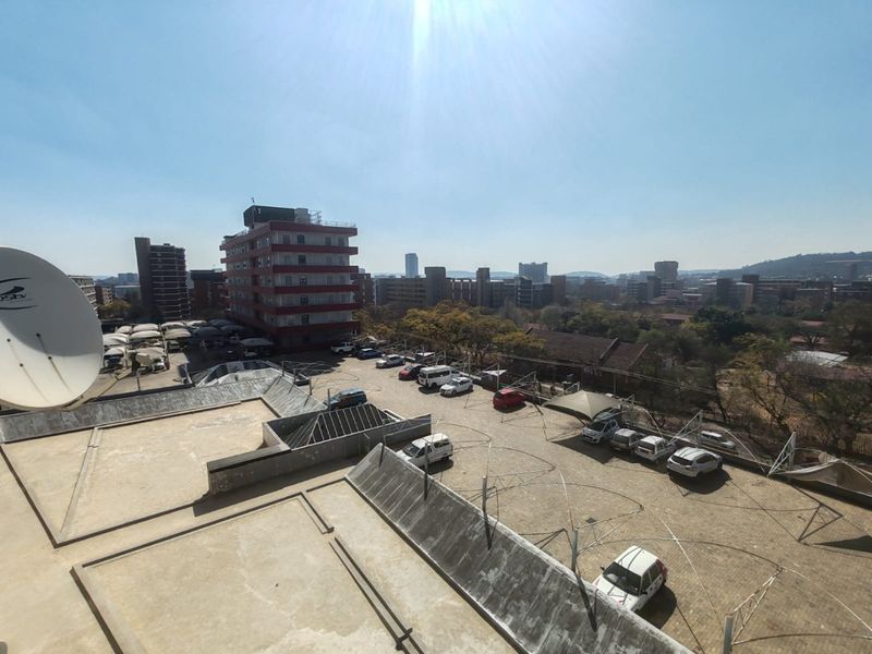 Elevated urban view overlooking a paved parking area with shade structures and surrounding apartment buildings under a clear sky.