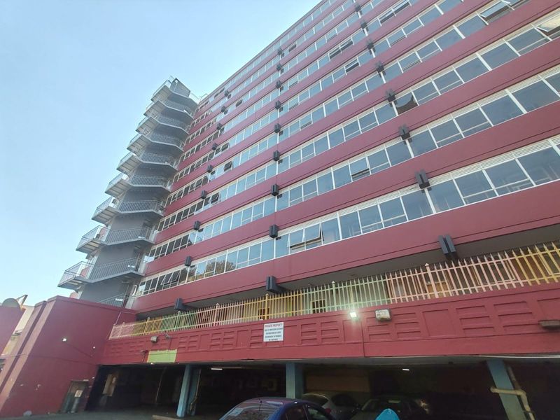 Low-angle view of a multi-story apartment building featuring an external fire escape staircase, security fencing, and ground-level undercover parking.