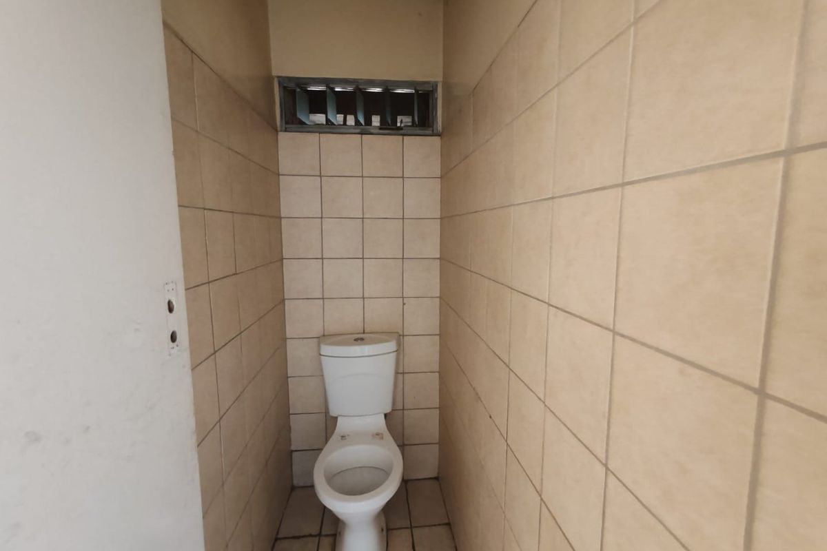A compact, tiled bathroom featuring a standard toilet and a small louvered window for ventilation, requiring cosmetic updates to improve its dated appearance.