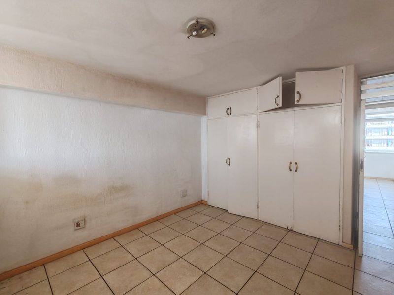 An empty bedroom featuring ceramic floor tiles and built-in cupboards, requiring cosmetic updates to the walls and cabinetry.