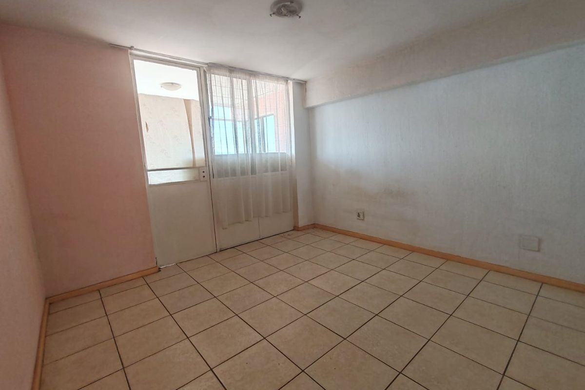 An empty bedroom featuring tiled flooring and direct access to a balcony through a glass door, requiring cosmetic updates to walls and finishes.