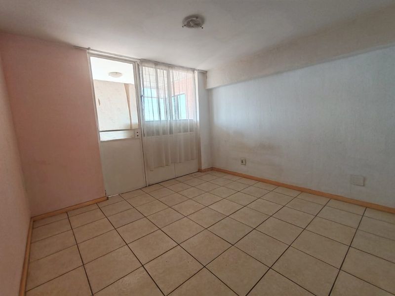 An empty bedroom featuring tiled flooring and direct access to a balcony through a glass door, requiring cosmetic updates to walls and finishes.