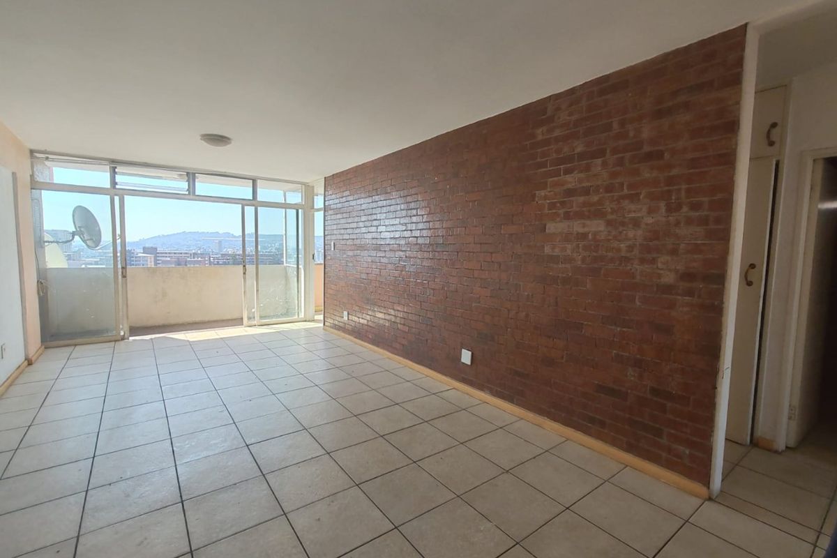 Spacious living area featuring an exposed brick feature wall, ceramic tiled flooring, and large sliding glass doors leading to a balcony with city views.