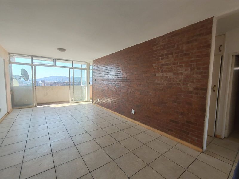 Spacious living area featuring an exposed brick feature wall, ceramic tiled flooring, and large sliding glass doors leading to a balcony with city views.