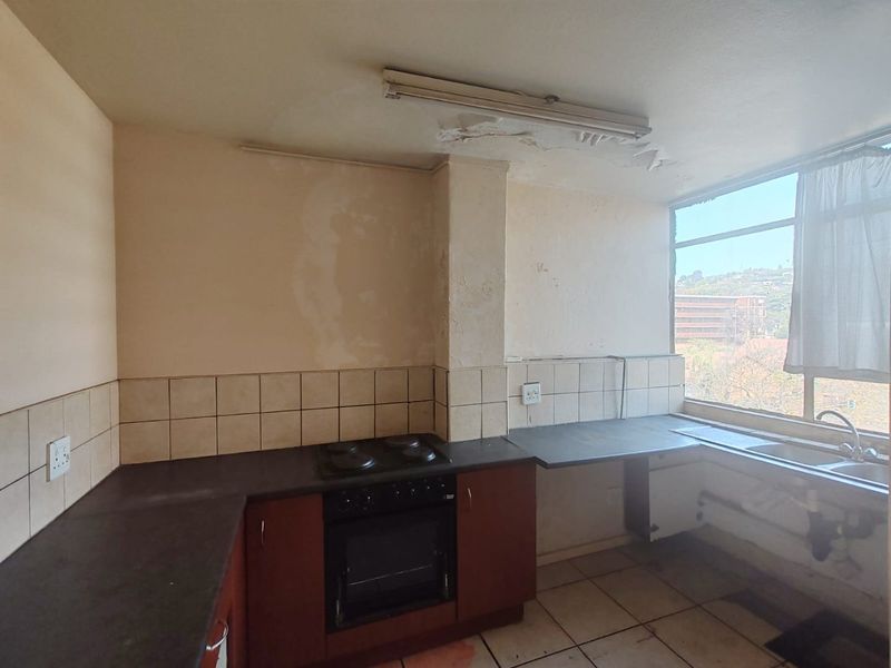 A dated kitchen featuring built-in cabinetry, an electric oven and hob, and tiled surfaces, currently requiring significant renovation and ceiling repairs.