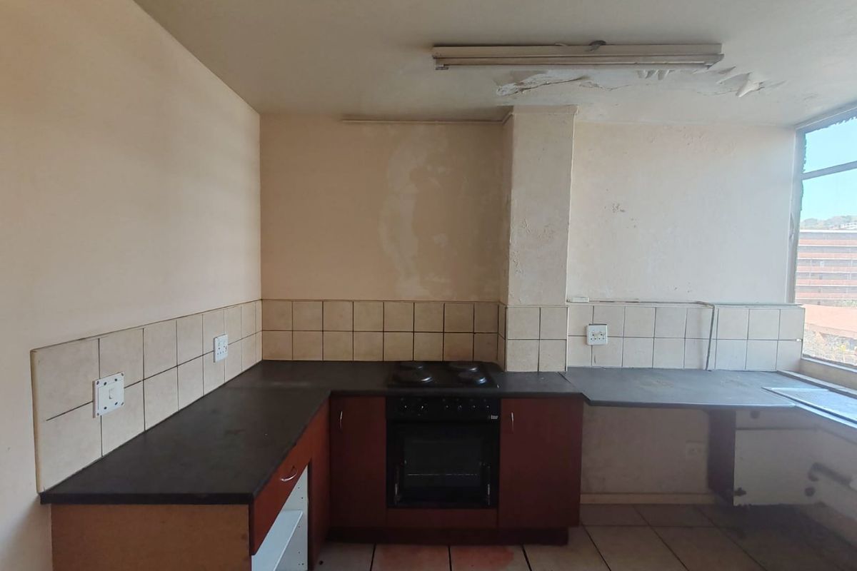 A dated kitchen featuring built-in cabinetry, an electric oven and hob, and tiled surfaces, currently requiring significant renovation and cosmetic repairs.