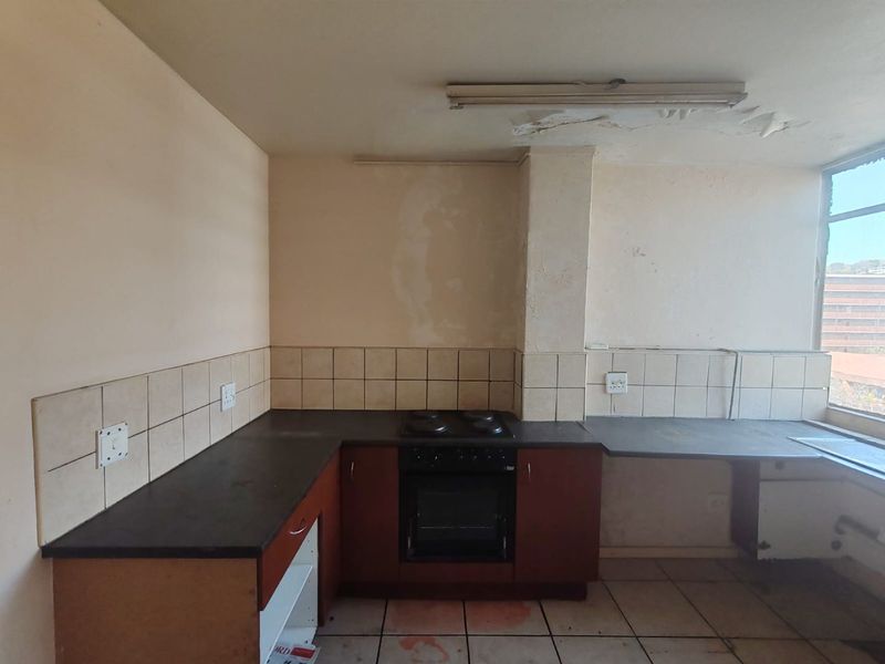 A dated kitchen featuring built-in cabinetry, an electric oven and hob, and tiled surfaces, currently requiring significant renovation and cosmetic repairs.
