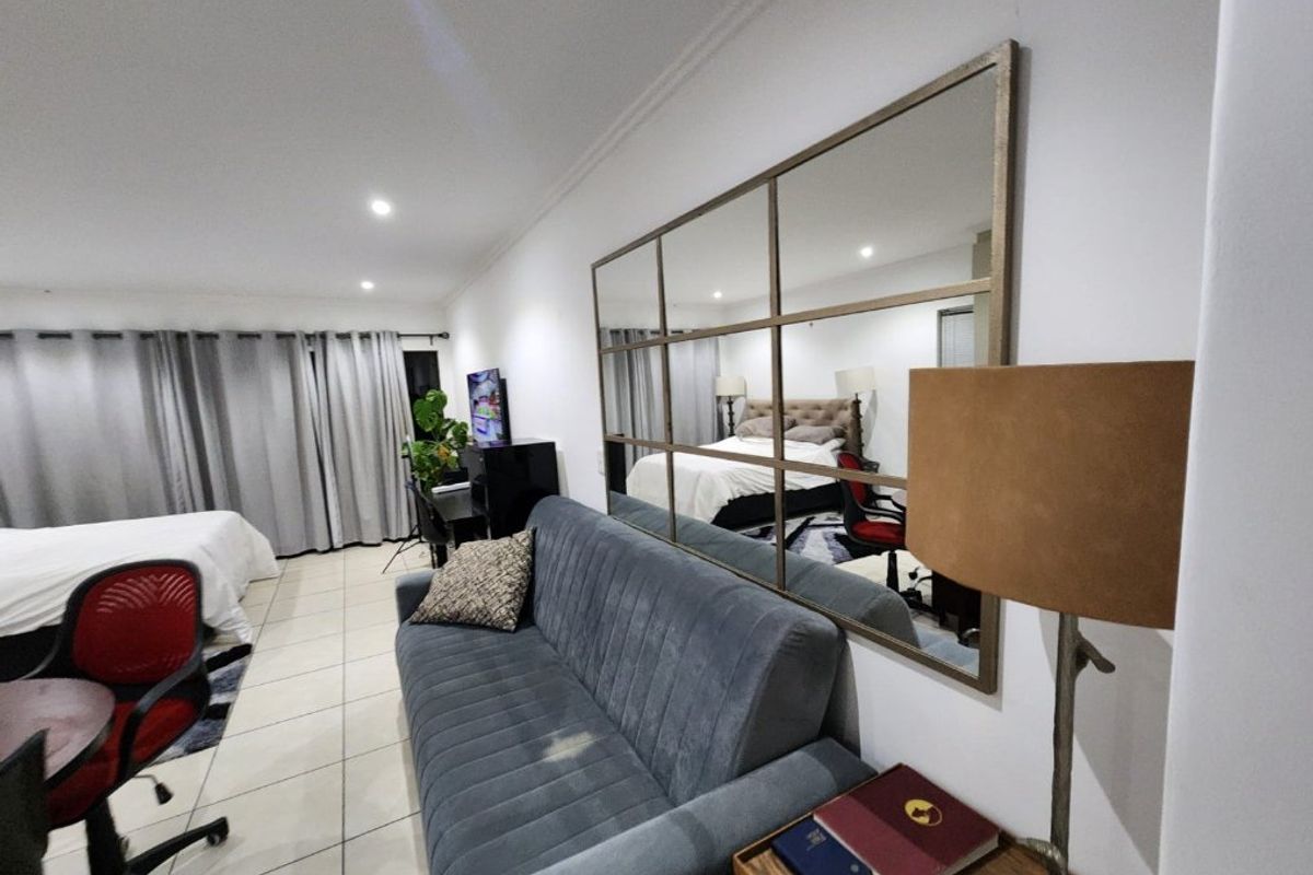 A spacious bedroom featuring tiled flooring, recessed downlighting, and large windows with curtain tracks, offering a comfortable and functional living space.