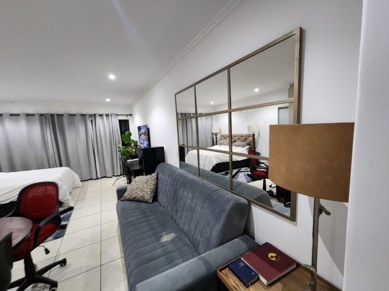 A spacious bedroom featuring tiled flooring, recessed downlighting, and large windows with curtain tracks, offering a comfortable and functional living space.