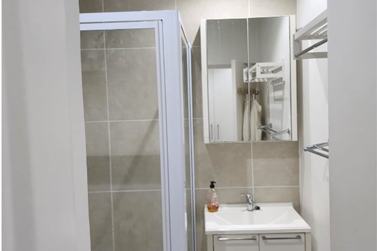 A compact, modern bathroom featuring a glass shower enclosure, a white vanity with basin, and a mirrored medicine cabinet with neutral wall tiling.