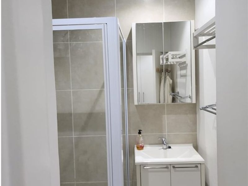 A compact, modern bathroom featuring a glass shower enclosure, a white vanity with basin, and a mirrored medicine cabinet with neutral wall tiling.