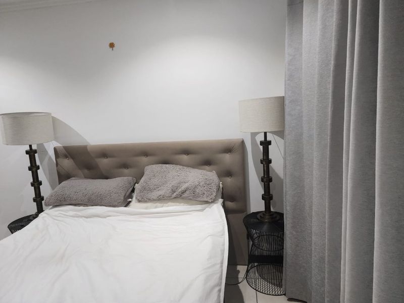 A bedroom featuring tiled flooring and neutral wall finishes, currently showing minor wall damage near the headboard area.