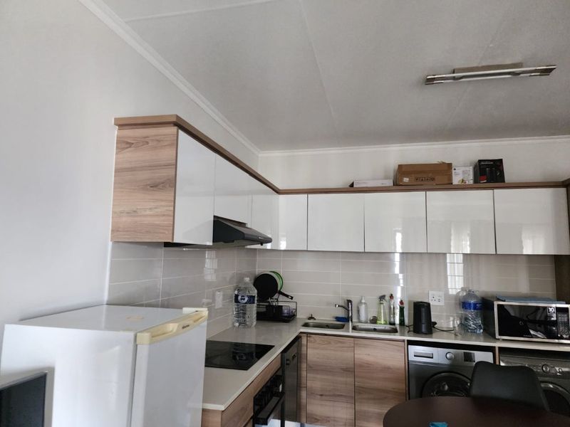 A functional kitchen featuring modern two-tone cabinetry, light-colored tiled backsplash, integrated hob, and stainless steel sink with ample counter space.
