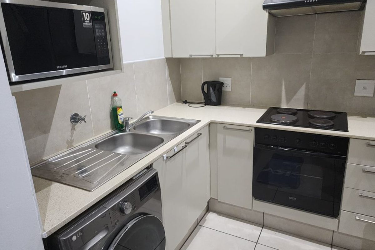Compact kitchen featuring fitted cabinetry, stone countertops, built-in oven, electric hob, extractor fan, and integrated microwave with tiled splashback.