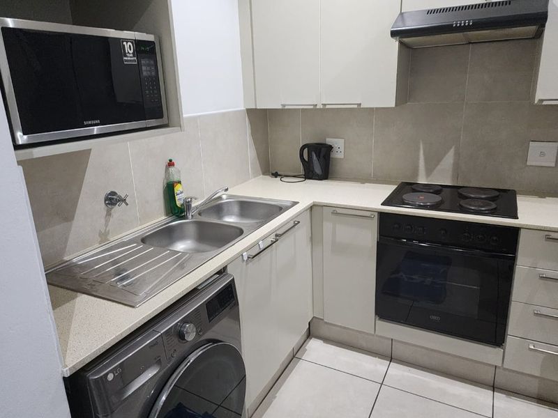 Compact kitchen featuring fitted cabinetry, stone countertops, built-in oven, electric hob, extractor fan, and integrated microwave with tiled splashback.