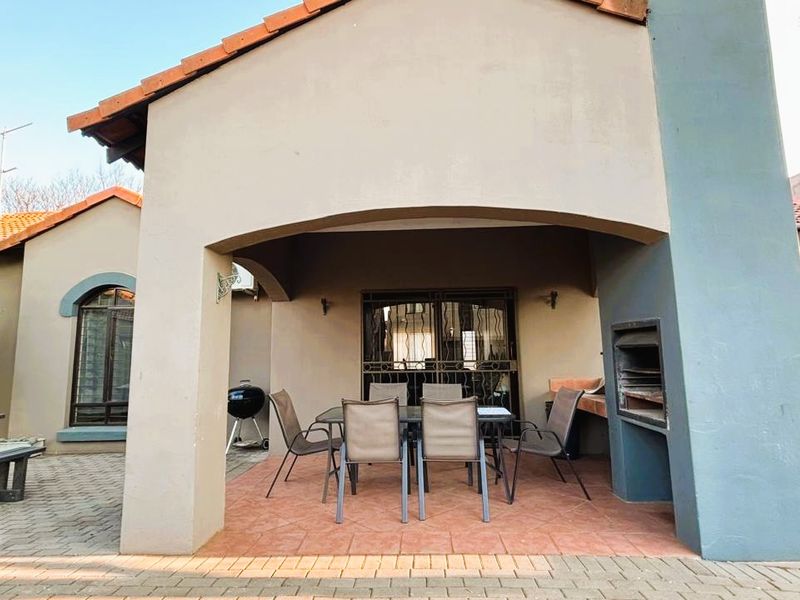 Covered patio area featuring a built-in braai, tiled flooring, and direct access to the home through a security gate.