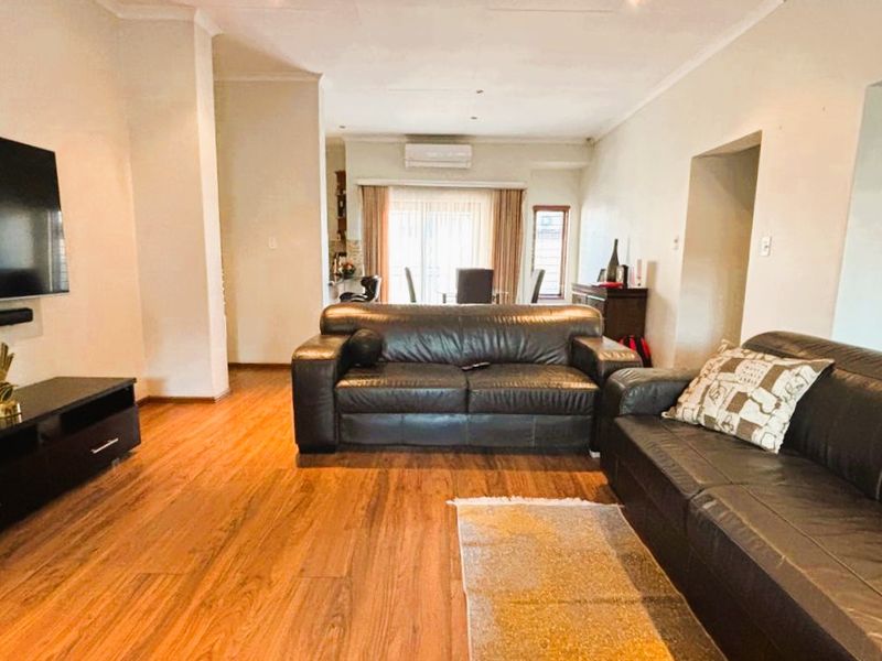 Spacious open-plan living area featuring warm laminate flooring, recessed lighting, and a wall-mounted air conditioning unit, creating a comfortable and functional living space.